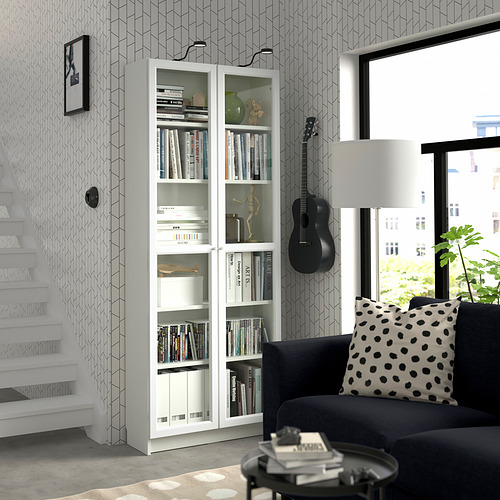 Sala de estar moderna con estantería blanca BILLY, sofá negro, ventana grande, soporte de pared para guitarra y decoración elegante.
