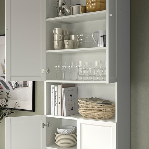 Estantería BILLY gris y blanca cuidadosamente organizada con cristalería, tazas, libros y cesta. Diseño sencillo y moderno.