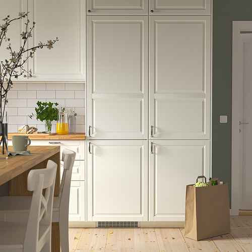 Cocina moderna con nevera TIAD, armarios blancos, encimera de madera, sillas y artículos. La nevera integrada cabe entre los armarios.