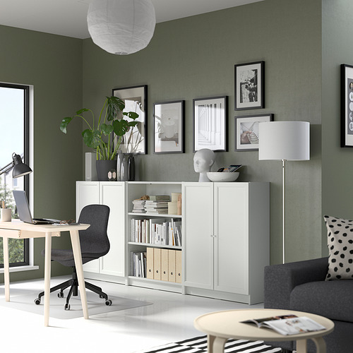 Sala de estar moderna con una estantería blanca BILLY y una silla gris contra paredes de color verde salvia, decorada con arte enmarcado y una lámpara blanca alta.