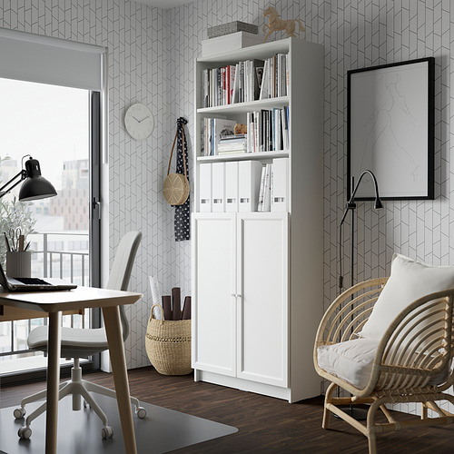 Sala de estar moderna con estantería blanca BILLY, silla de madera, escritorio, lámpara y decoración de pared.
