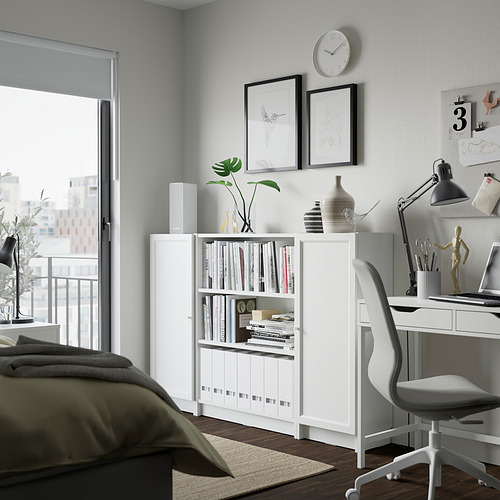Moderna oficina en casa con estantería blanca BILLY con estantes abiertos llenos de libros y artículos decorativos. Incluye escritorio, silla blanca y arte de pared.