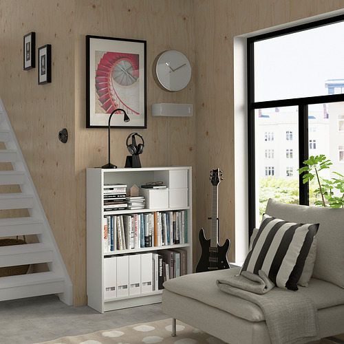 Sala de estar moderna con estantería BILLY, guitarra, sofá gris, almohadas, ventana y arte minimalista.