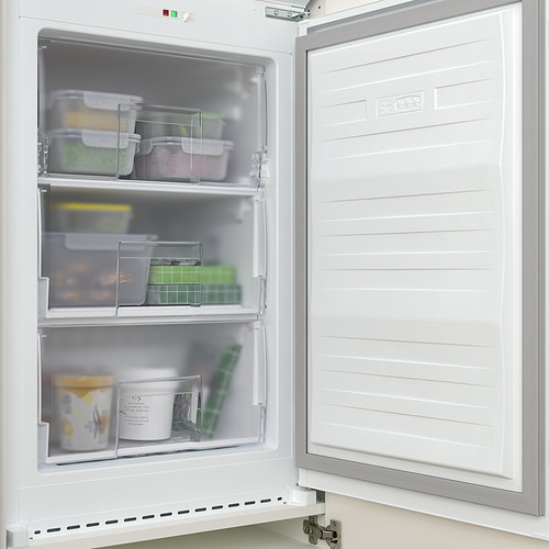 Congelador integrado blanco abierto con cajones transparentes que revelan los alimentos. Colocado dentro de un armario a juego.