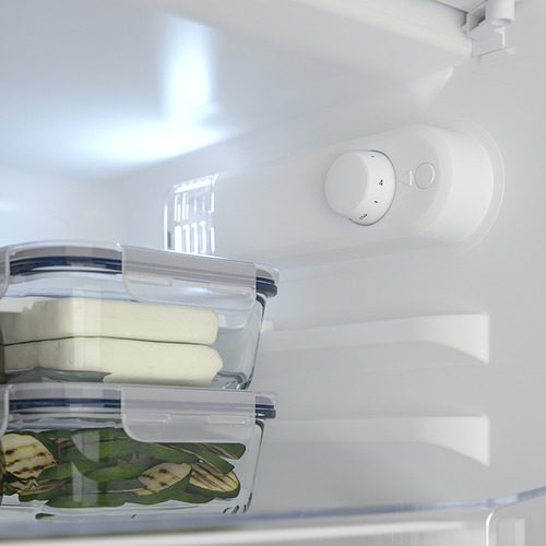 Interior de la nevera TYLLSNÄS con estante ajustable completo que contiene un recipiente de plástico con lonchas de queso y otro recipiente con pepinos en rodajas.