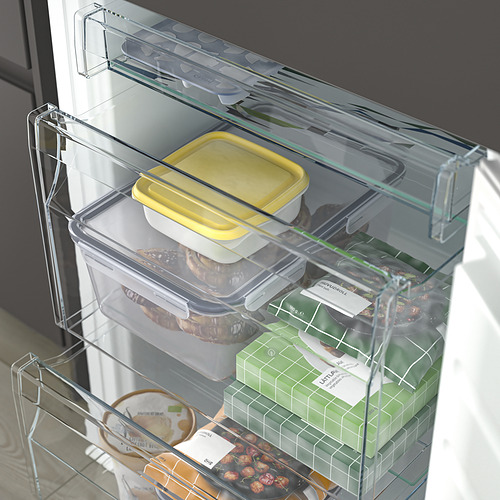 Una nevera moderna con estantes de vidrio transparentes ajustables que muestran varios alimentos como un contenedor amarillo, nueces y productos verdes empaquetados.