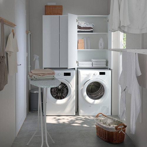 Lavadero moderno con unidades de almacenamiento NYSJÖN blancas sobre lavadoras blancas. Puertas, estanterías y una cesta de mimbre con la ropa.
