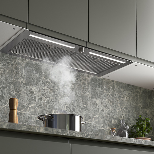 Cocina moderna con campana de acero inoxidable que emite vapor, integrada sobre salpicadero de mármol, iluminada y funcional.