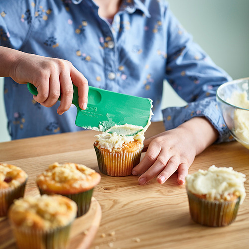 Una persona que usa la espátula verde SJÖRUDA para glasear cupcakes con precisión.
