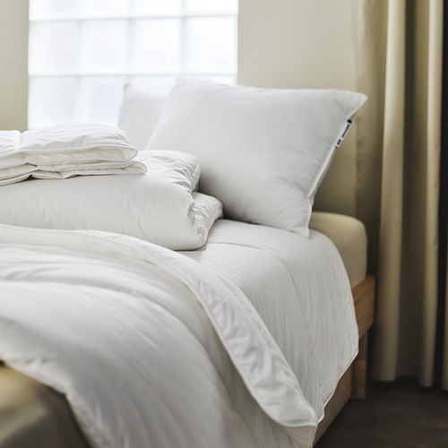 Cama grande y pulcramente hecha con edredón y almohadas SKOGSFRÄKEN blancas, iluminación suave y esponjosa, brillante.