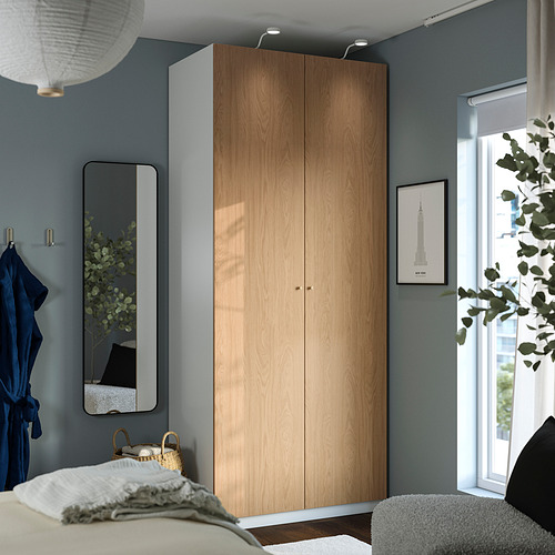 Acogedor dormitorio con armario PAX de madera clara, pared azul, espejo gris y arte vibrante. Confortable con alfombra blanca y sillón gris.