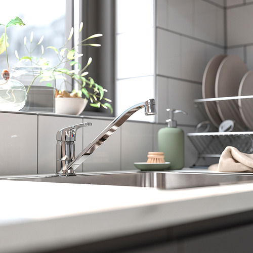 Moderno grifo de cocina cromado con diseño elegante, dispensador de jabón verde y pequeña planta en fregadero con azulejos grises.