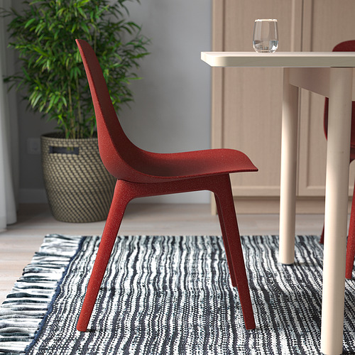 Silla roja de curvas suaves y patas de madera, fácil de montar, colocada cerca de una mesa con un vaso.