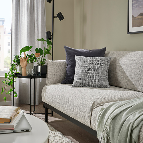 Sala de estar con cojín JORDKASTANJ gris, ordenador portátil, libros, planta y decoración minimalista.