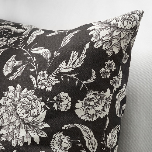 Almohada negra con diseño floral blanco, detalles intrincados, tela lisa, vista de lado.