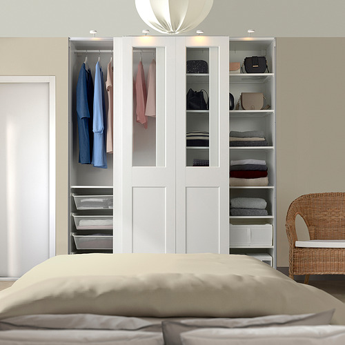 Modern bedroom with large white storage unit, open sections showing clothes and folded garments, neat beige bedding in front. Illumination from above.