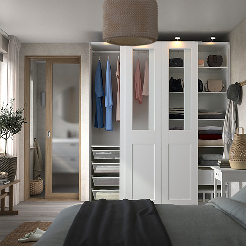 Modern bedroom with white PAX wardrobe, hanging clothes, shelves, and open storage. Black blanket, wicker baskets, and plants create cozy space.