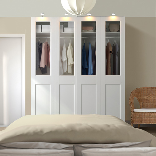 Armario blanco PAX con ropa colorida, cama grande y silla de mimbre.