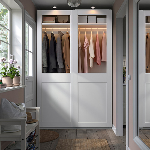 Armario PAX con puertas de cristal, paneles blancos, ropa cuidada.