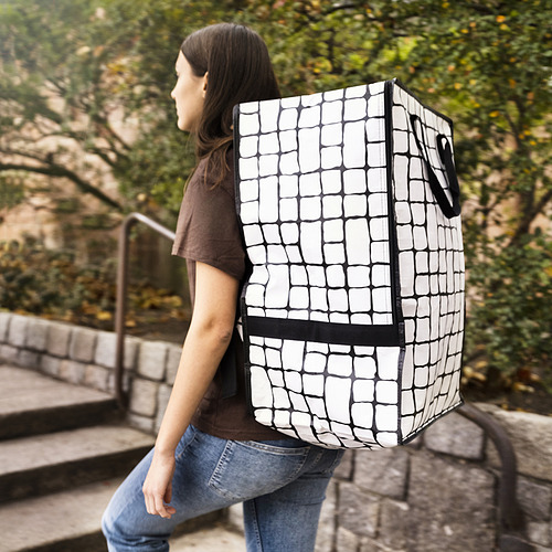 Una persona que lleva una mochila GÖRSNYGG en blanco y negro, más grande que las mochilas típicas, diseñada para transportar o mover grandes cargas.