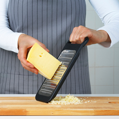La persona ralla el queso en una herramienta de cocina negra con superficie de acero y base estable.