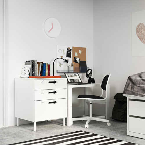 Moderna habitación para niños con arcón y escritorio SMÅSTAD blancos, silla negra, decoración colorida, alfombra a rayas y reloj grande.