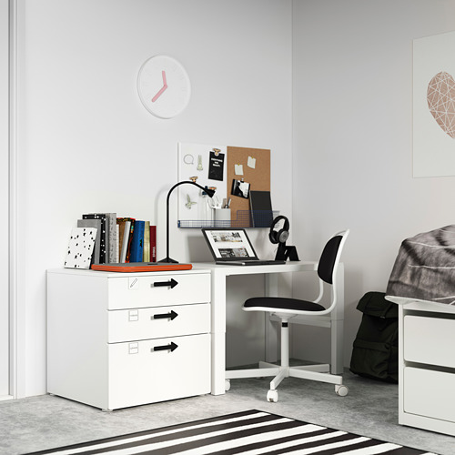 Pequeño escritorio blanco en el dormitorio, silla gris, portátil, libros, lámpara, mochila, alfombra a rayas, reloj, carteles.