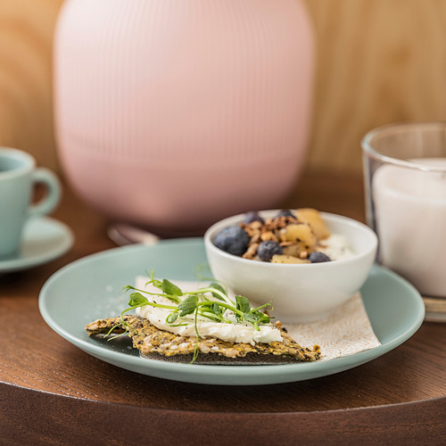 Un plato lateral verde con comida y un vaso sobre una mesa de madera. El plato es sencillo y funcional, diseñado para combinar con otras vajillas.