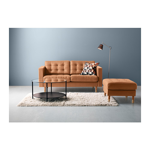 Moderna configuración de sala de estar con sofá naranja, reposapiés a juego, mesa de centro de vidrio y lámpara de pie contra pared azul.