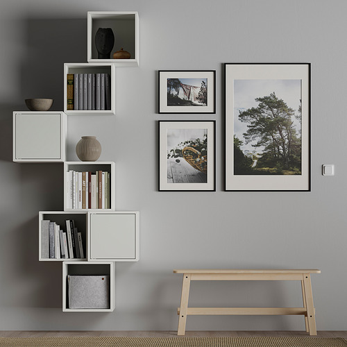 Habitación moderna con paredes grises, estanterías modulares blancas y fotos. Los estantes contienen libros, un jarrón y una canasta. Banco de madera debajo.