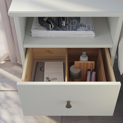 Mesita de noche blanca IDANÄS con cajón y estante que exhibe libros y objetos pequeños.