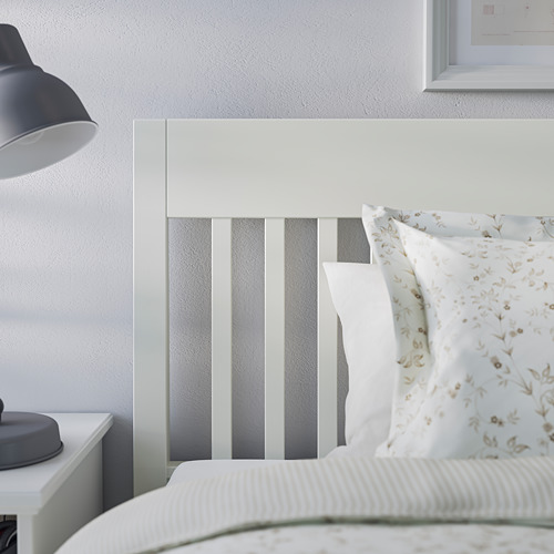 Cama blanca con paneles grises, almohadas florales, lámpara gris en mesita de noche.