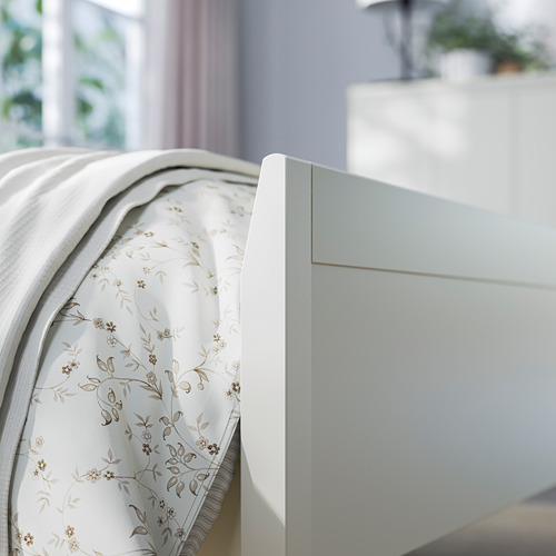 Esta imagen muestra un marco de cama IDANÄS azul claro con intrincado lecho floral, sobre un sereno fondo de habitación.