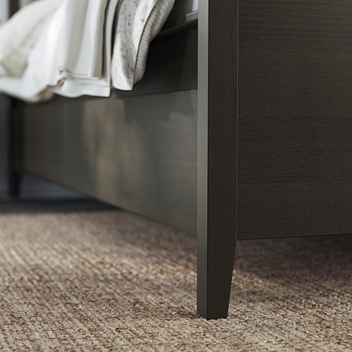 Mueble de madera oscura pata debajo de una cama con sábanas blancas.