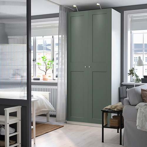 Habitación moderna con armario PAX, gris verdoso, alta, cerca de la ventana, rodeada de muebles blancos y sofá gris.