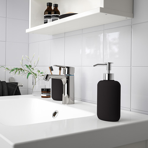 El moderno soporte para cepillos de dientes EKOLN negro se encuentra cerca del grifo cromado en un elegante mostrador de baño blanco. Pequeño, elegante y funcional.