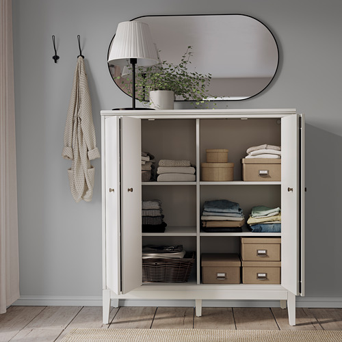 Armario de almacenamiento organizado IDANÄS con puertas plegables, blancas, que contienen ropa, cajas y libros. Elegante y funcional.