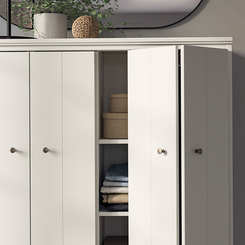 Un armario IDANÄS blanco con puertas abiertas que dejan ver la ropa doblada. Es una unidad moderna y elegante con perillas redondas, ideal para el almacenamiento.