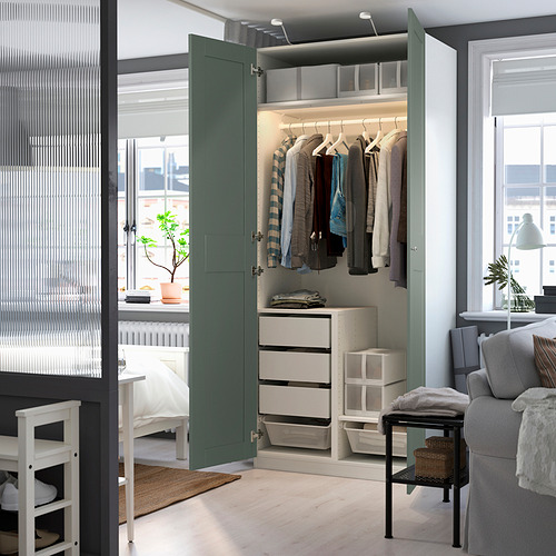 Un armario PAX verde con puertas abiertas revela la ropa en perchas, cajones y estantes, mostrando su espacio interior organizado para las prendas.