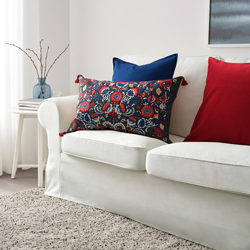 Sofá blanco con una gran almohada floral azul marino y rojo, almohadas más pequeñas sólidas de color marino y rojo, jarrón azul con ramas en la mesa auxiliar.