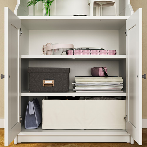 Armario de almacenamiento HAUGA blanco abierto, organizado con varios artículos como libros, bolsos y cajas en estantes.