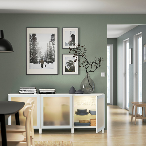 Comedor moderno con aparador BESTÅ, puertas de vidrio con platos, jarrón y fotos.