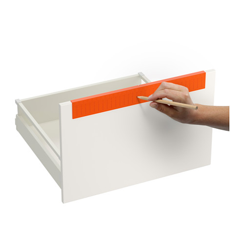 Persona usando una plantilla de taladro naranja para marcar la posición en el cajón blanco para una colocación precisa de la manija.