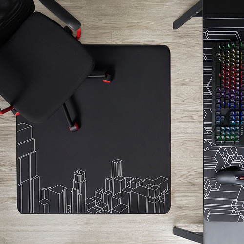 Silla negra de tres patas sobre una alfombrilla abstracta de paisaje urbano junto a un teclado colorido.