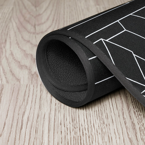 Alfombrilla de silla de juego enrollable negra con patrón geométrico, que muestra su parte inferior texturizada para mayor estabilidad.