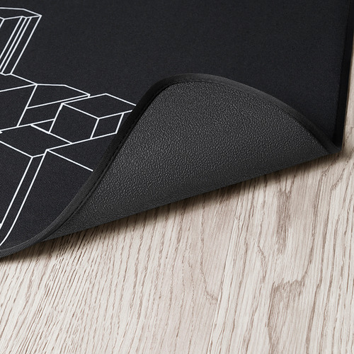 Alfombrilla negra para silla de juego con diseño geométrico blanco, respaldo de goma gruesa y duradera, colocada sobre piso de madera.