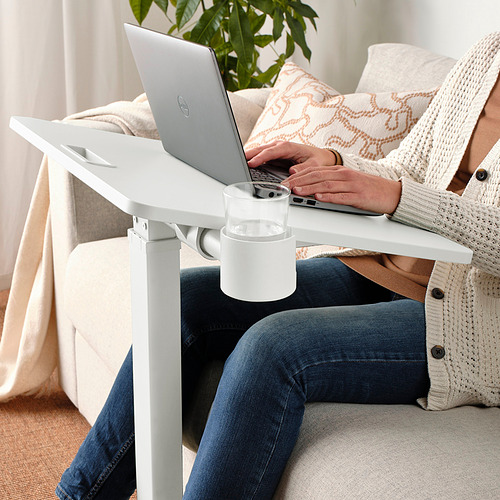 Persona sentada en un sofá usando una mesa de computadora portátil ajustable en altura con un portavasos.