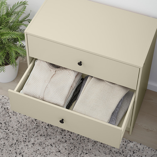 Cómoda abierta de color crema con tres toallas cuidadosamente dobladas en el cajón inferior. Plante junto a él sobre una alfombra.