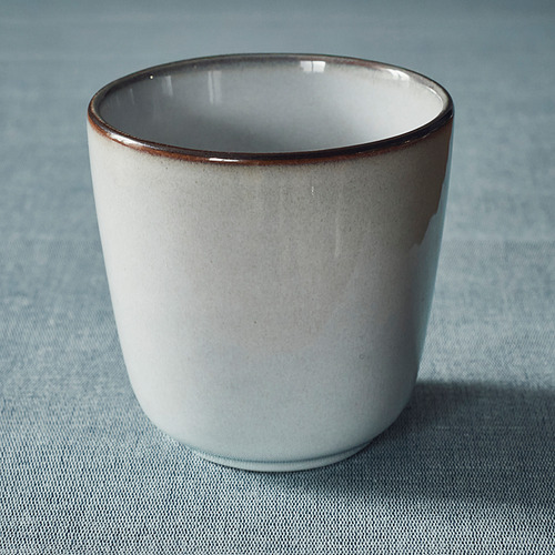 Taza blanca con borde marrón sobre superficie azul.