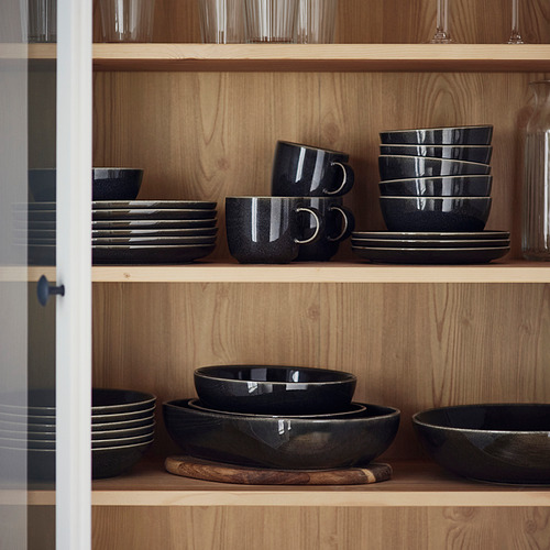 Platos GLADELIG negros en estantes de madera; platos, cuencos, tazas limpias y ordenadas, glaseado oscuro, formas limpias.